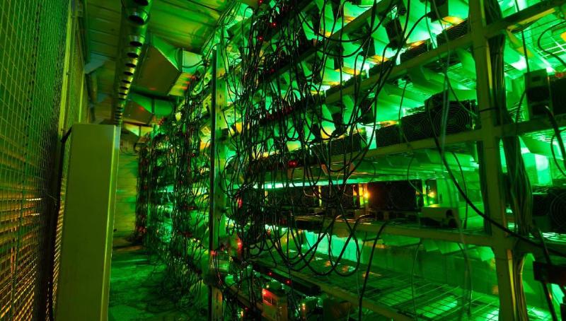 An image of Bitcoin miners stacked in a large warehouse with green lighting