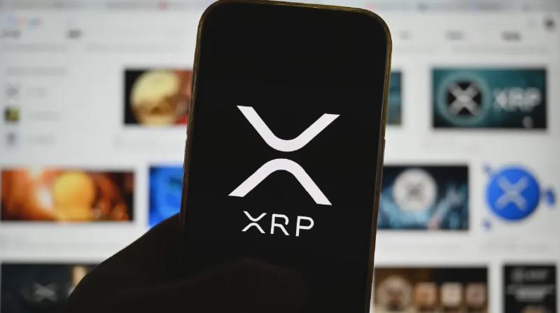 Een afbeelding van het logo van cryptomunt XRP op een mobiele telefoon met op de achtergrond veel content van de munt